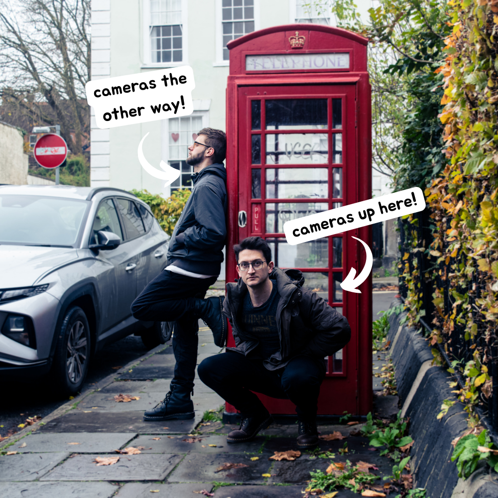 Luke and Archie from Walking Billboards pose next to a red telephone booth. Luke looks away from the camera while Archie crouches down. A popout over Luke reads 'cameras the other way!'. A popout over Archie reads 'cameras up here!'